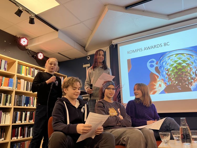 en gruppe mennesker som sitter i et rom med en stor skjerm